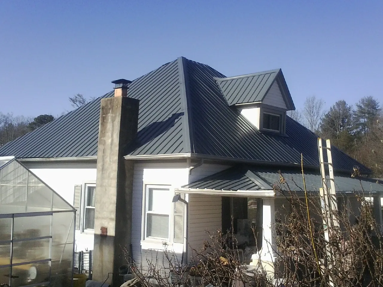 Dark blue standing seam metal roof on a white farmhouse with dormer — Slate & Tile Roof Repair by Roofing Brothers in Wentworth