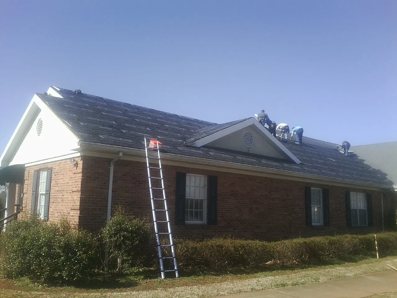 Crew tearing shingles off a brick ranch roof with a ladder set — Metal Roof Repair work by our crew in Wentworth