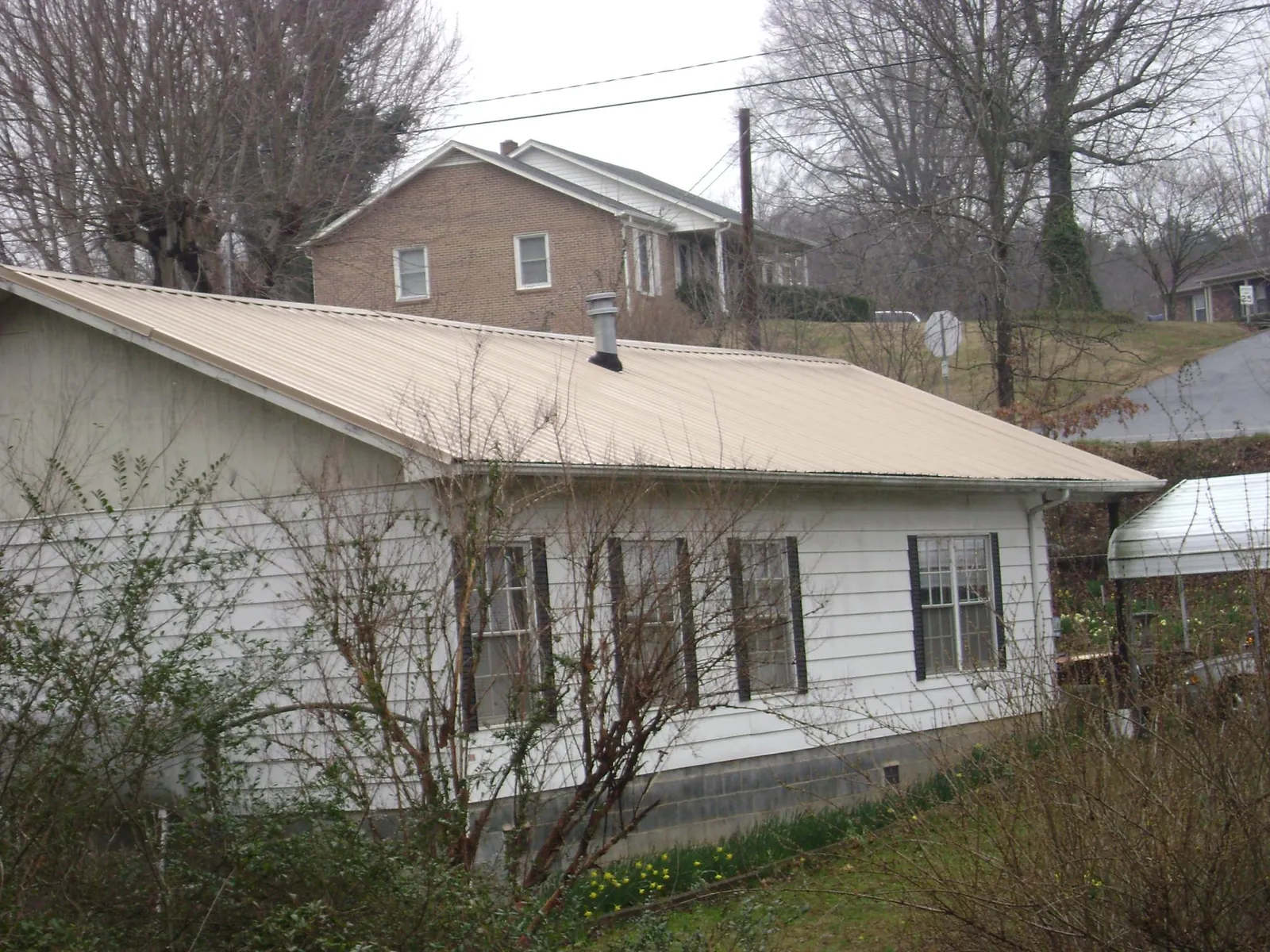 Tan metal roof on a white sided house set into a hillside — Commercial Roofing by Roofing Brothers in Wentworth