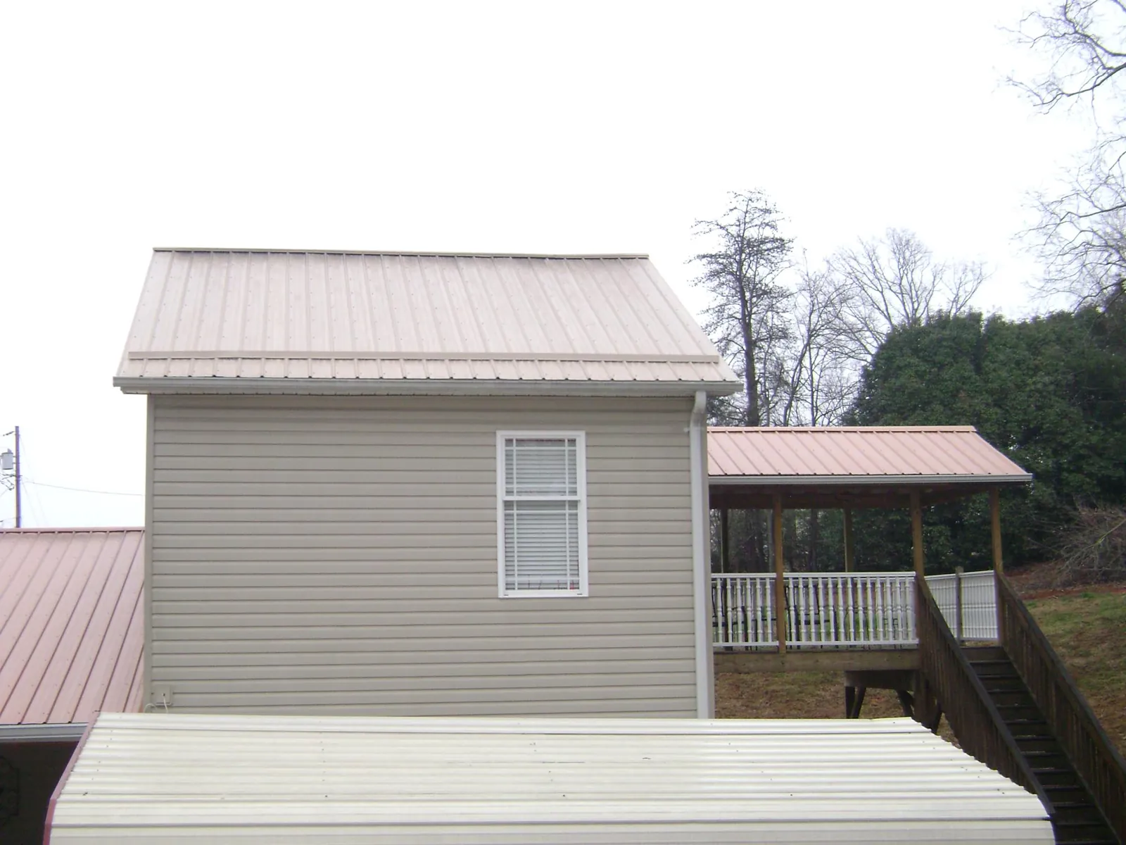 Tan metal roofs on a two story addition and attached porch, from a Roof Replacement job in Wentworth
